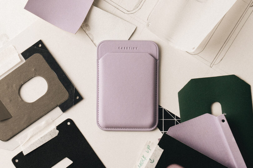 Purple leather phone wallet surrounded by paper and fabric samples on a table.