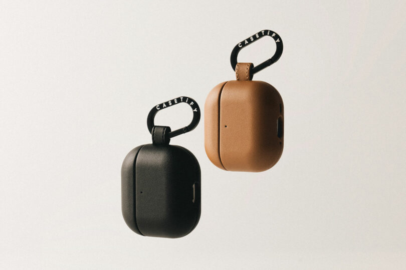 Two AirPods cases, one black and one brown, with sleek loop keychains prominently showcasing the "CASETiFY" label, elegantly set against a neutral background.