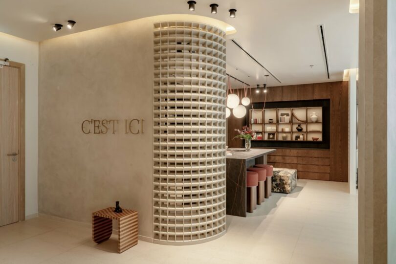 Modern interior with a curved lattice wall, a table with red cushioned stools, and wall shelving. 