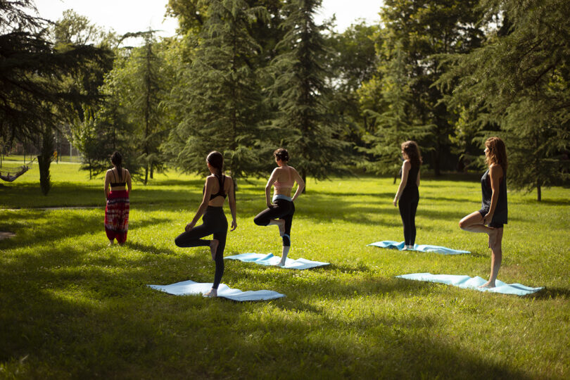 Five people practicing yoga on blue mats in a grassy park at Lopota Lake Resort, surrounded by trees under golden sunlight.