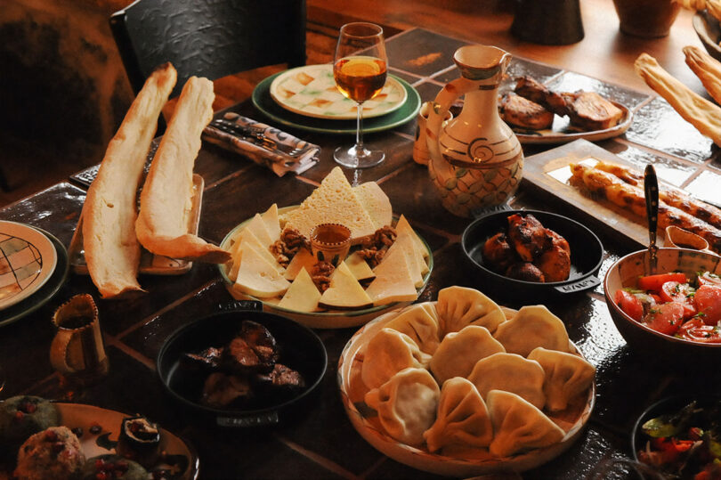 A table set with various dishes, including bread, dumplings, cheese, meat, and a glass of wine, reminiscent of a delightful feast at Lopota Lake Resort.