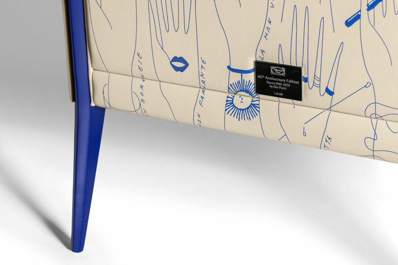 Close-up of a chair leg with blue illustrations on beige fabric, featuring hands and text. A black label reads 