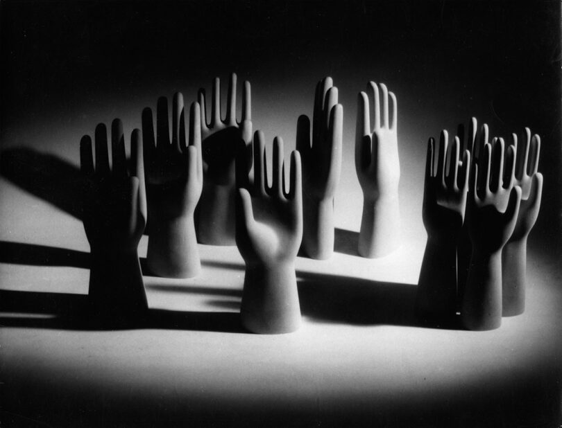 Monochrome image of multiple upright mannequin hands, reminiscent of Gio Ponti's elegant forms, arranged in a group and casting dramatic shadows on a flat surface.