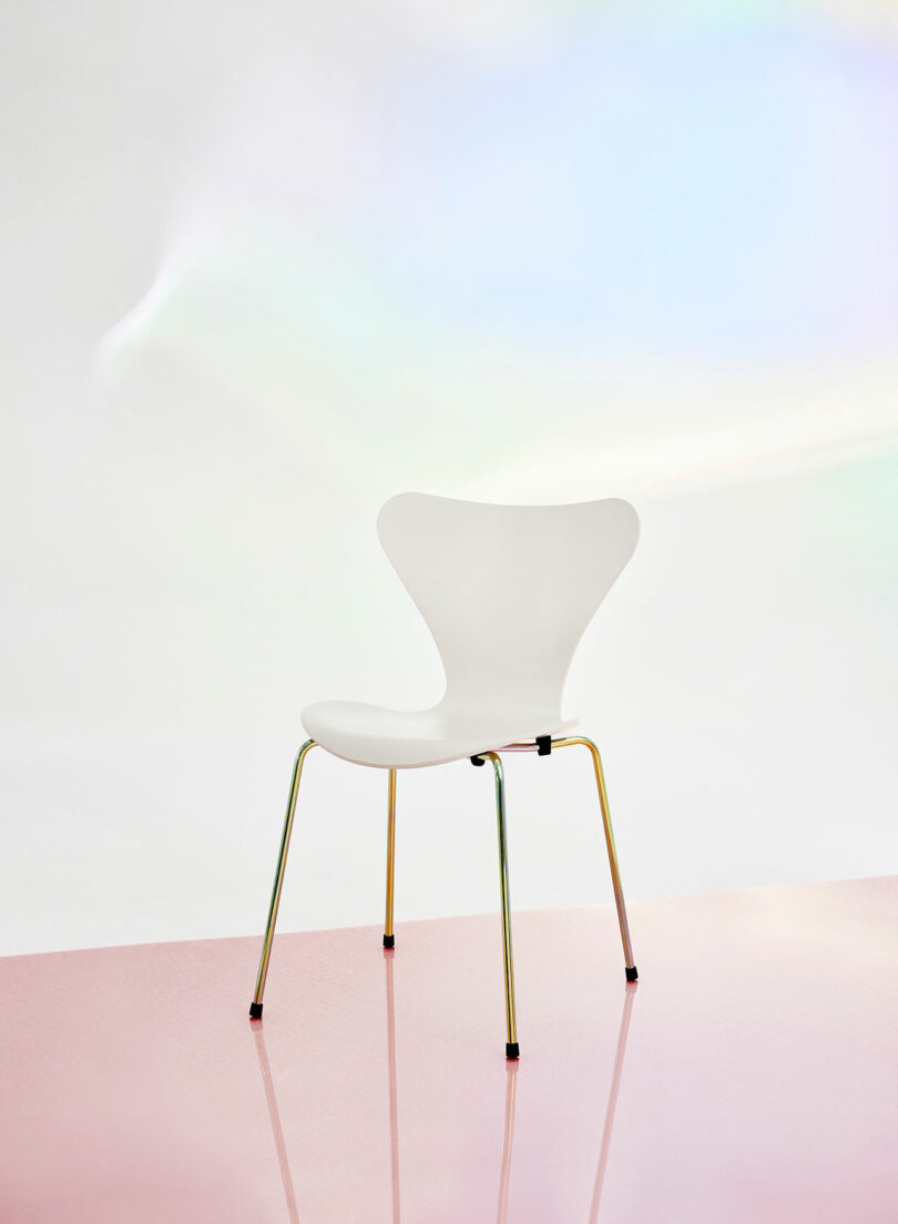 A white chair with metallic legs on a glossy pink surface against a soft gradient background.