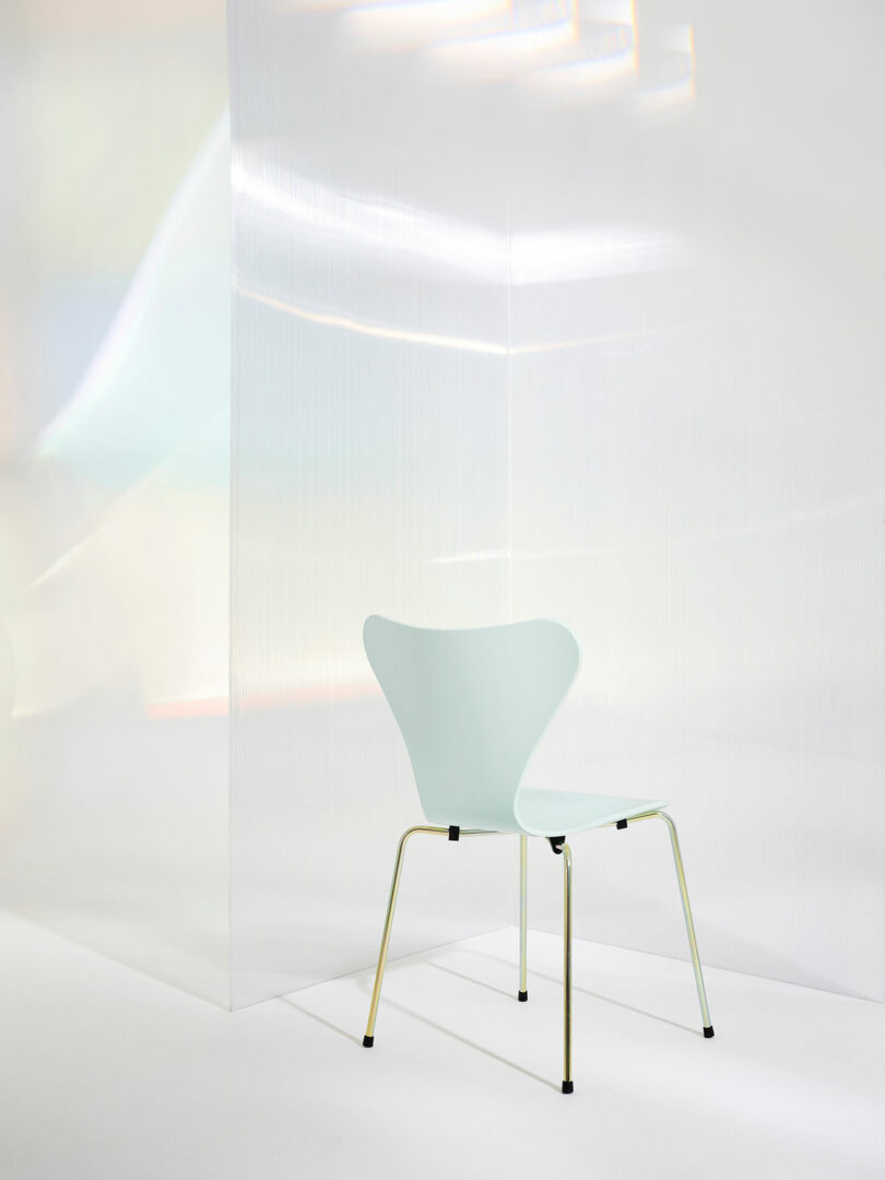 A minimalist chair with a light blue seat and thin metal legs is placed in a softly lit, abstract setting with translucent panels.