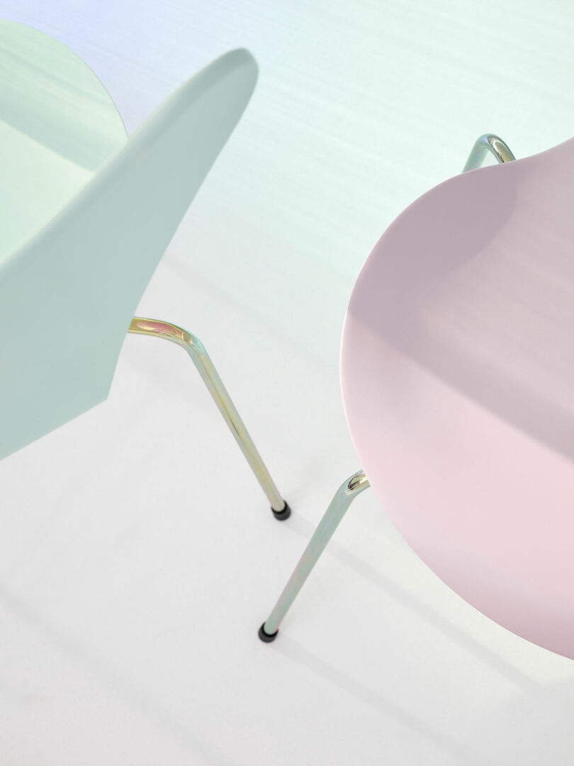 Two modern chairs with curved backs and metal legs on a light background. One chair is pale green, and the other is pale pink.