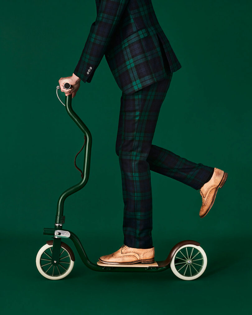 Person wearing a green plaid suit and brown dress shoes riding a green scooter against a green background.