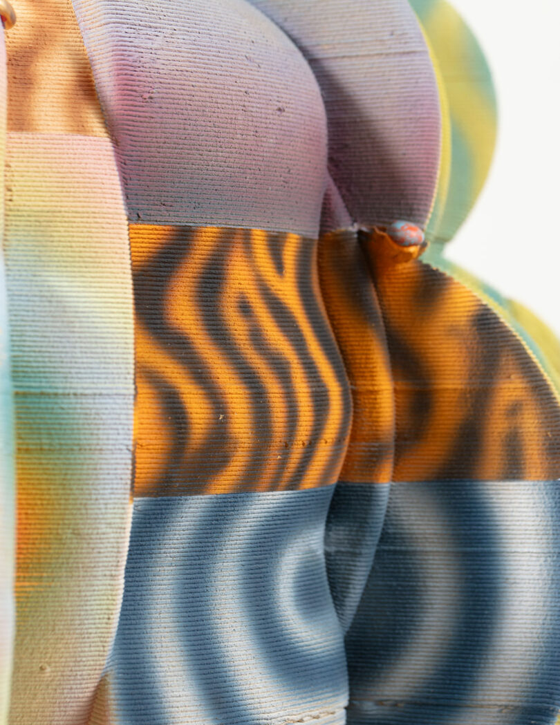 Close-up of a fabric with colorful spray-painted patterns, including waves and circles in orange, blue, and pink hues.