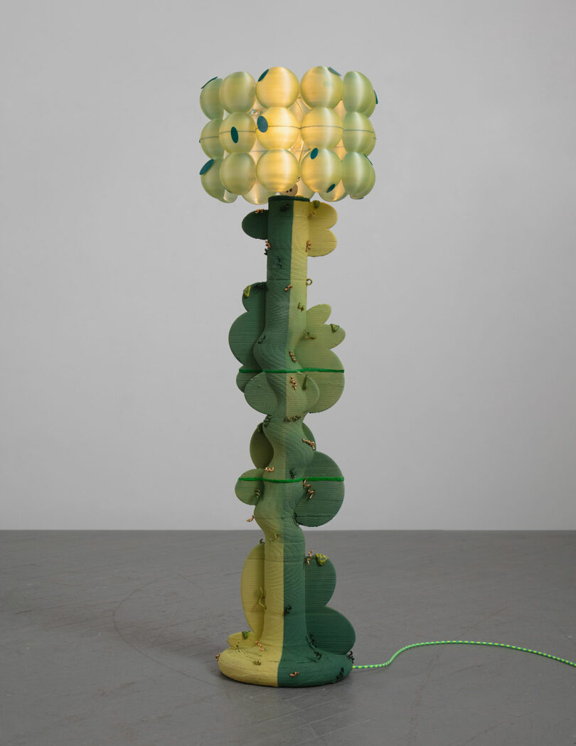 A uniquely designed green floor lamp with a spherical, bubble-like shade and a green cord on a gray floor.