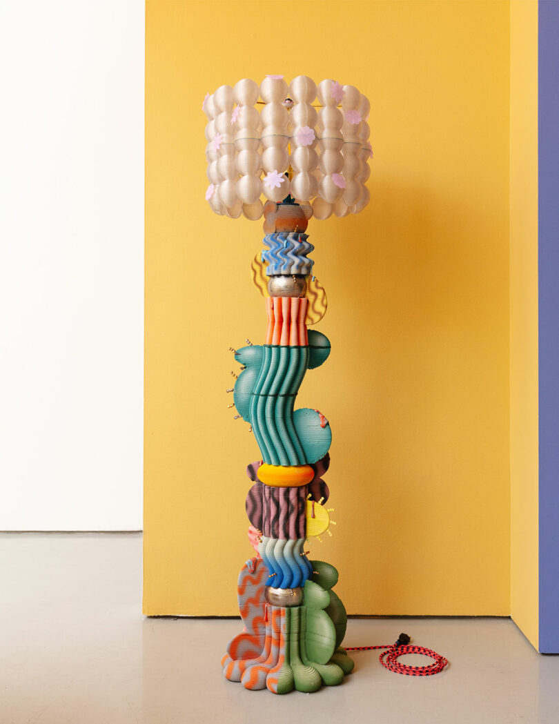 A colorful, sculptural floor lamp with a textured base and a cloud-like lampshade stands against a yellow wall.