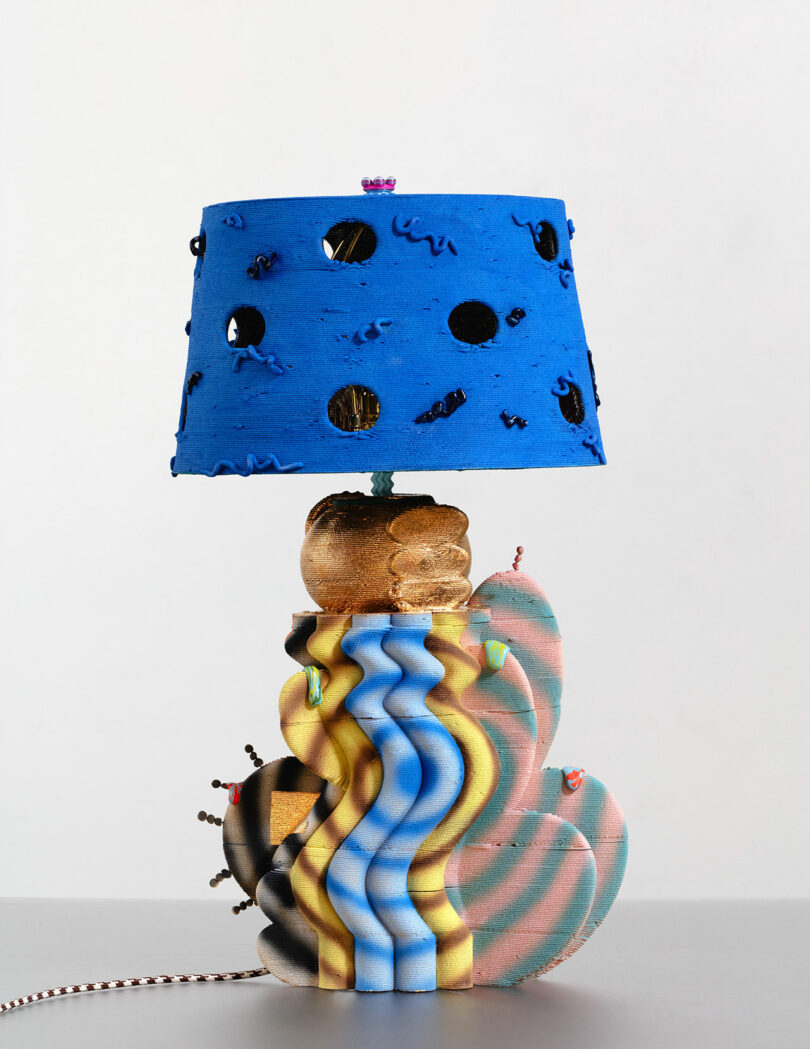 A lamp with a colorful, abstract base featuring wavy patterns, topped by a blue lampshade with black dots and small decorative elements.