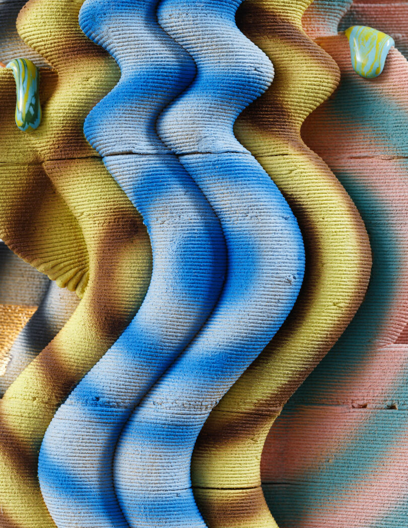 Abstract pattern with wavy, textured shapes in blue, yellow, and orange, resembling layered clay or fabric.