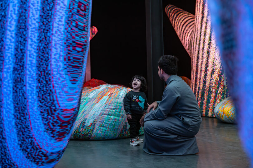 Un enfant et un adulte interagissent au milieu de grandes sculptures textiles colorées dans un espace de galerie.