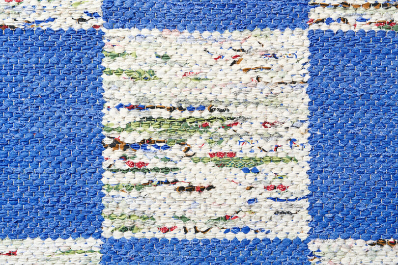 Frank in the Loom presents a woven rug with a blue and white checkered pattern, showcasing small multicolored details within the white squares.