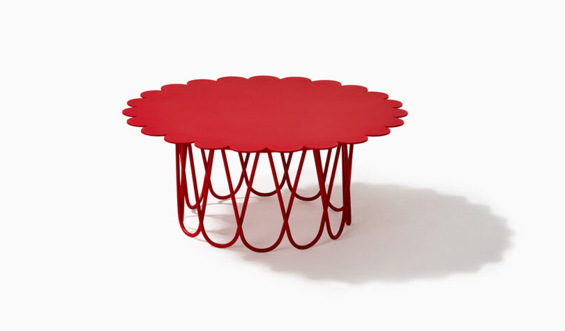 A red, round table with a scalloped edge and open lattice base on a white background.