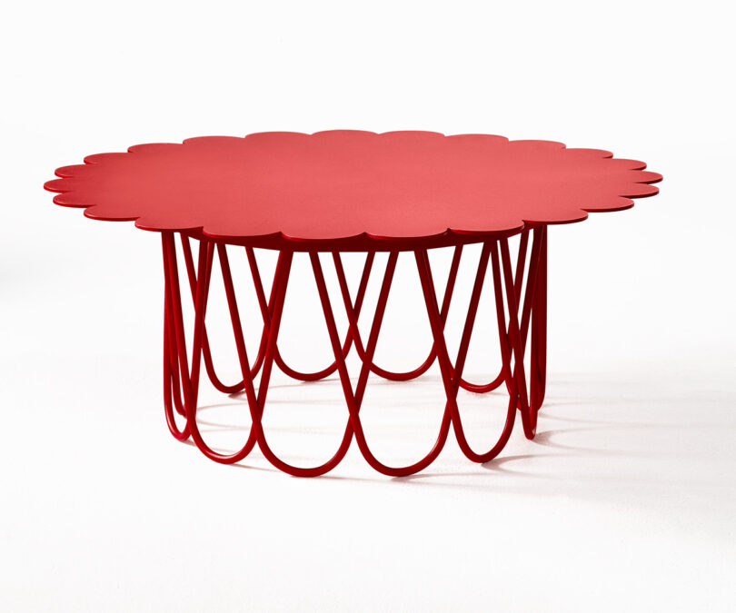 A red, circular table with a scalloped edge and an intertwined wire base, placed on a white background.