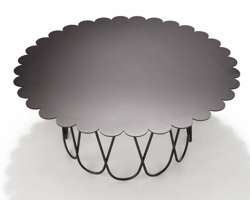 A round coffee table with a scalloped edge and a metal wireframe base, placed on a light-colored surface.