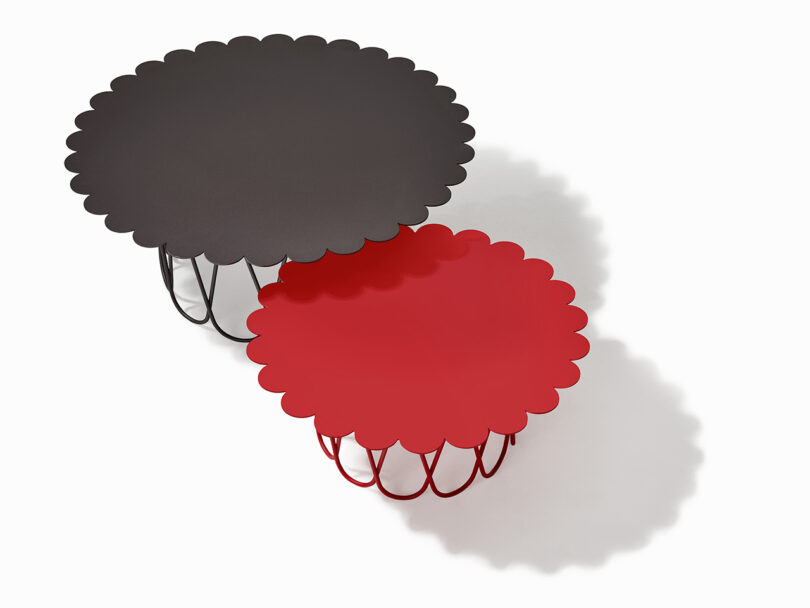 Two round tables with scalloped edges, one black and one red, featuring intertwined wire legs on a white background.