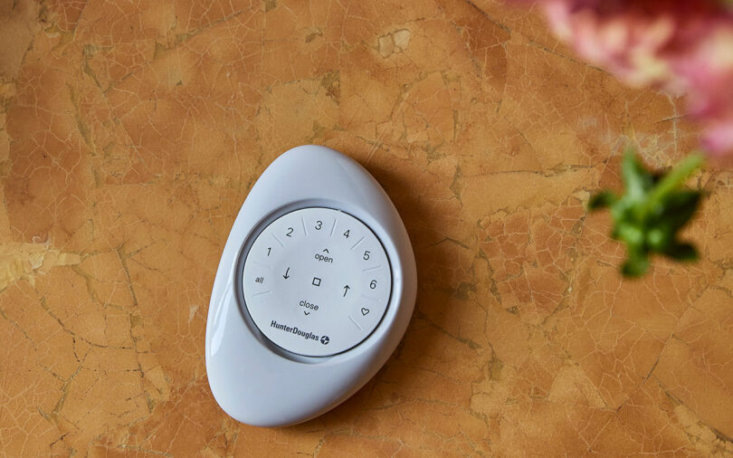 A white, oval-shaped remote control with buttons sits on a marbled surface.