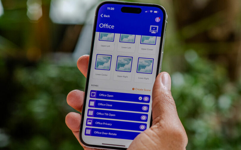 Hand holding smartphone displaying an app interface for controlling office settings, featuring options like Office Open, Office Close, and scene selections with a nature background.