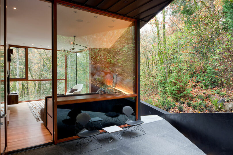 Habitación moderna con paredes de vidrio con acentos de madera y muebles minimalistas, con vistas a una exuberante vista al bosque.