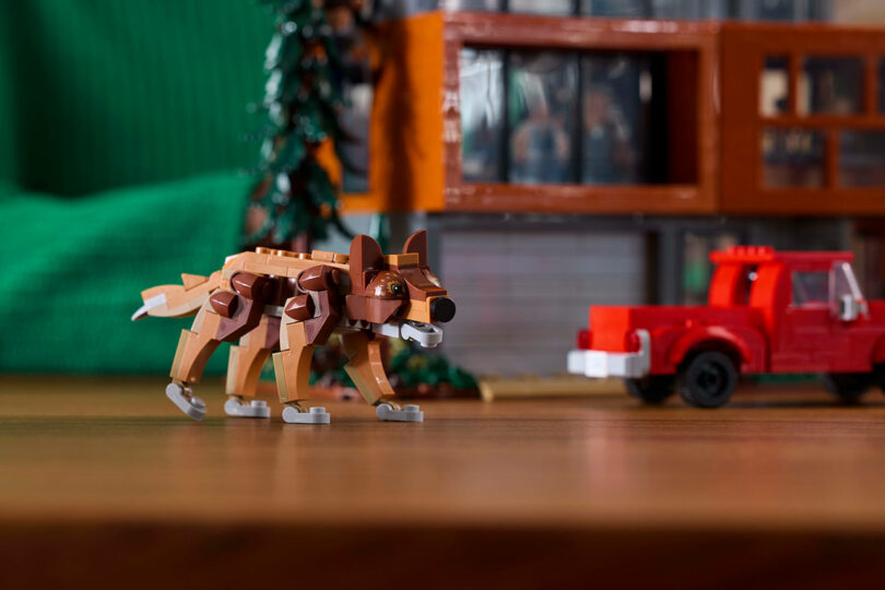 Una modelo de LEGO Wolf se encuentra en una superficie de madera frente a un camión rojo Lego y un árbol de Lego.