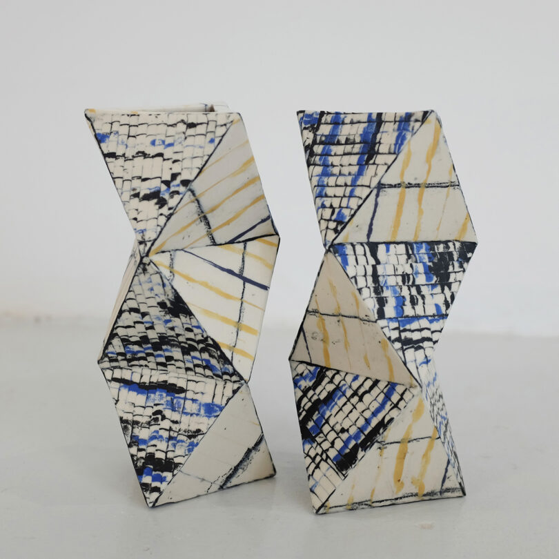 Deux sculptures en céramique géométrique avec des formes angulaires et un motif de mosaïque dans des tons noirs, bleus et beige, situés sur un fond simple.