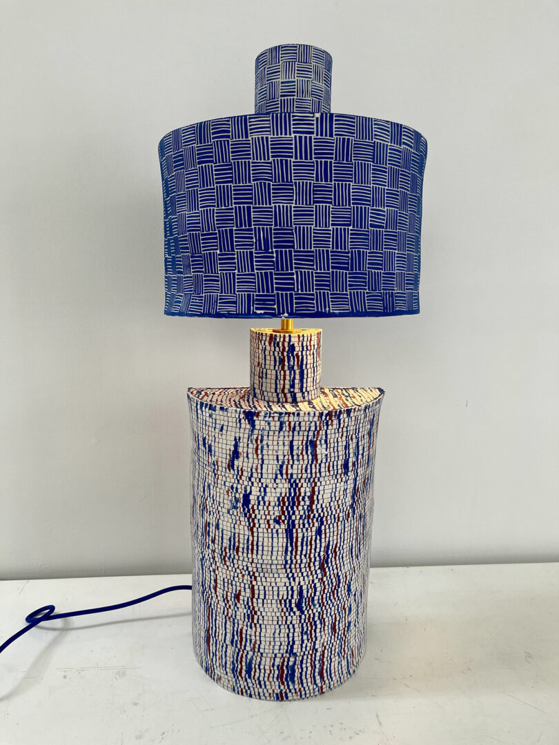 Lampe de table avec une teinte à motifs bleus et une base multicolore texturée sur un fond blanc.