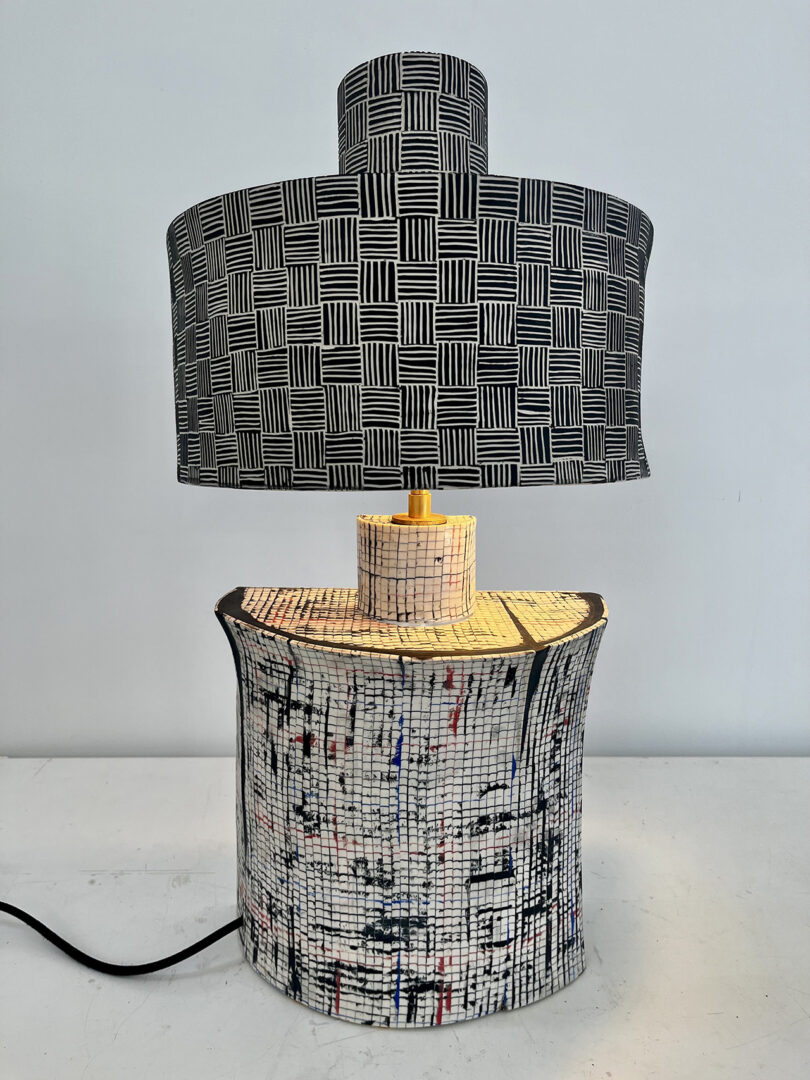 Une lampe de table avec une teinte noire et blanche à motif de grille et une base multicolore texturée.