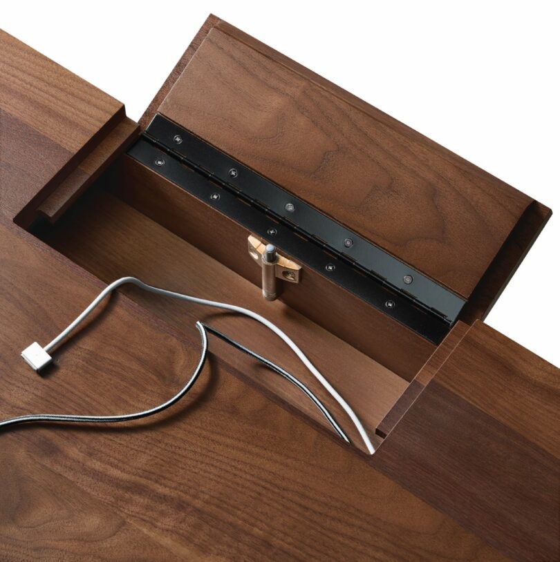 Close-up of a wooden desk with a concealed compartment open, showing two cords, one with a USB connector.