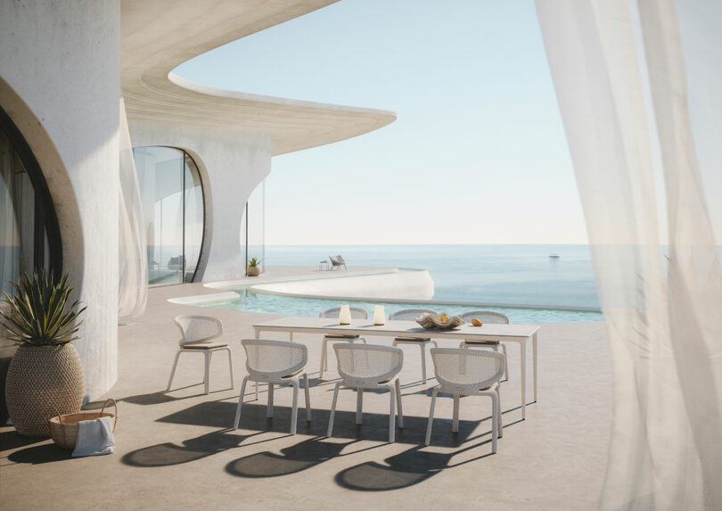 Modern white patio overlooking the ocean with a DEDON dining set and a small pool. Curved architectural design and airy curtains enhance the serene coastal atmosphere.