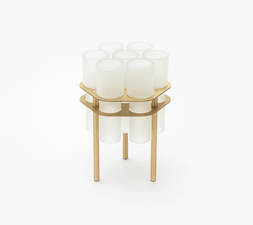 A modern side table with a glass top, supported by cylindrical frosted glass pillars and gold-colored legs.