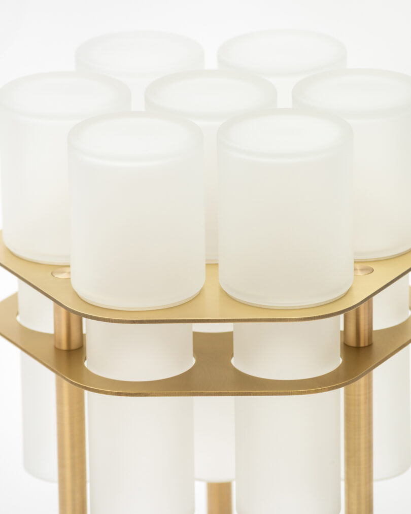 A close-up of a modern lamp with nine frosted cylindrical glass shades on a gold metallic frame.