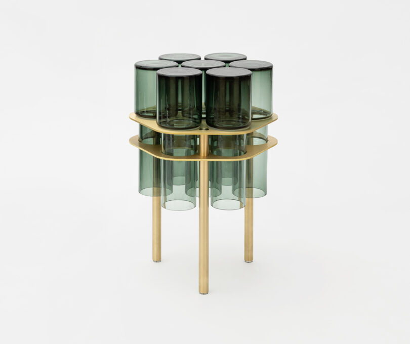 A modern side table with a gold metal frame and a top made of cylindrical green glass pieces.