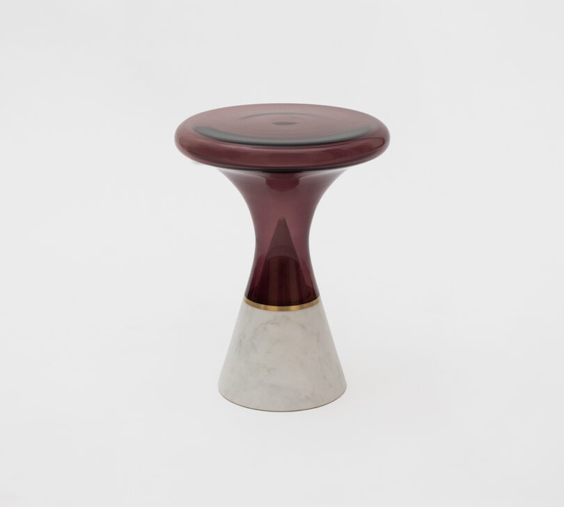 A modern stool with a burgundy, glossy seat and a beige, cone-shaped base on a plain white background.