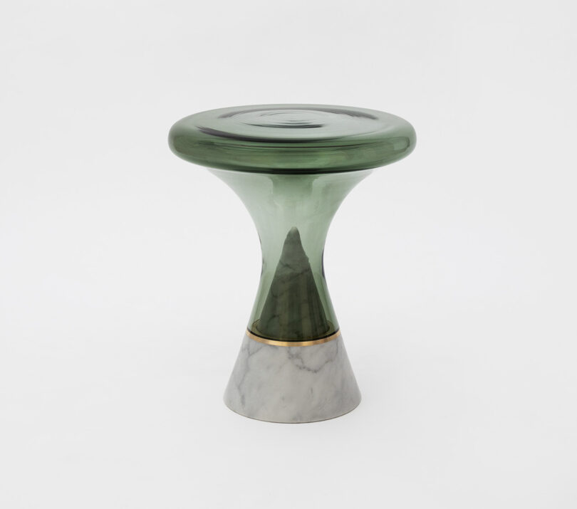 A modern stool with a green glass seat and a conical marble base, featuring a distinct transition from the glass to the marble through a gold accent band.