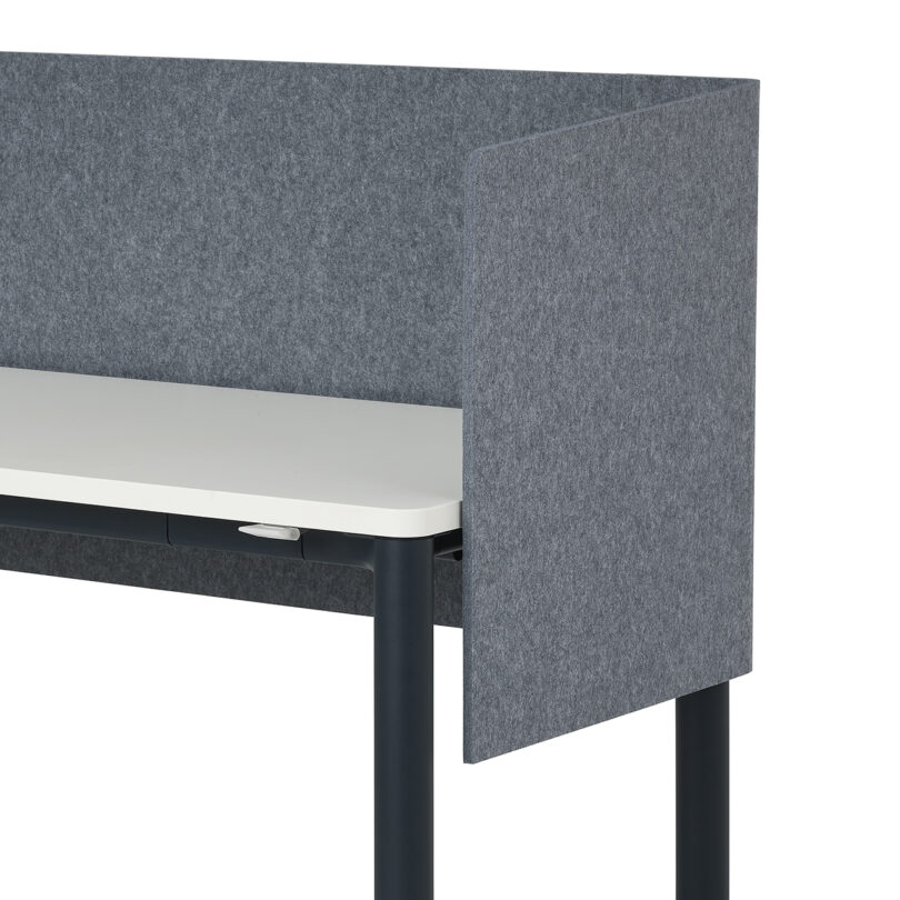 A desk with a white tabletop and dark legs features a gray fabric privacy panel surrounding three sides.