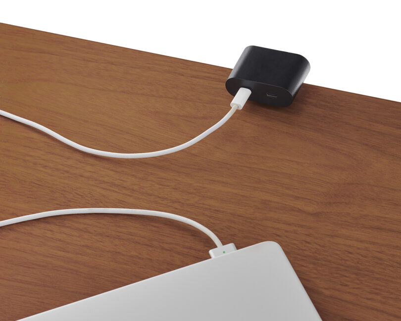 A USB-C charger is plugged into a laptop, which is partially visible on a wooden surface.