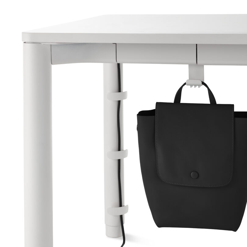 White desk with a cable organizer and a black bag hanging on a hook.