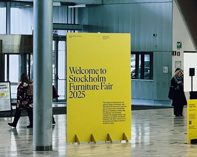 A vibrant yellow sign proudly announces "Welcome to Stockholm Furniture Fair 2025" in sleek black lettering, set against a contemporary indoor backdrop. Attendees stroll leisurely in the background, eager to explore the latest design innovations.