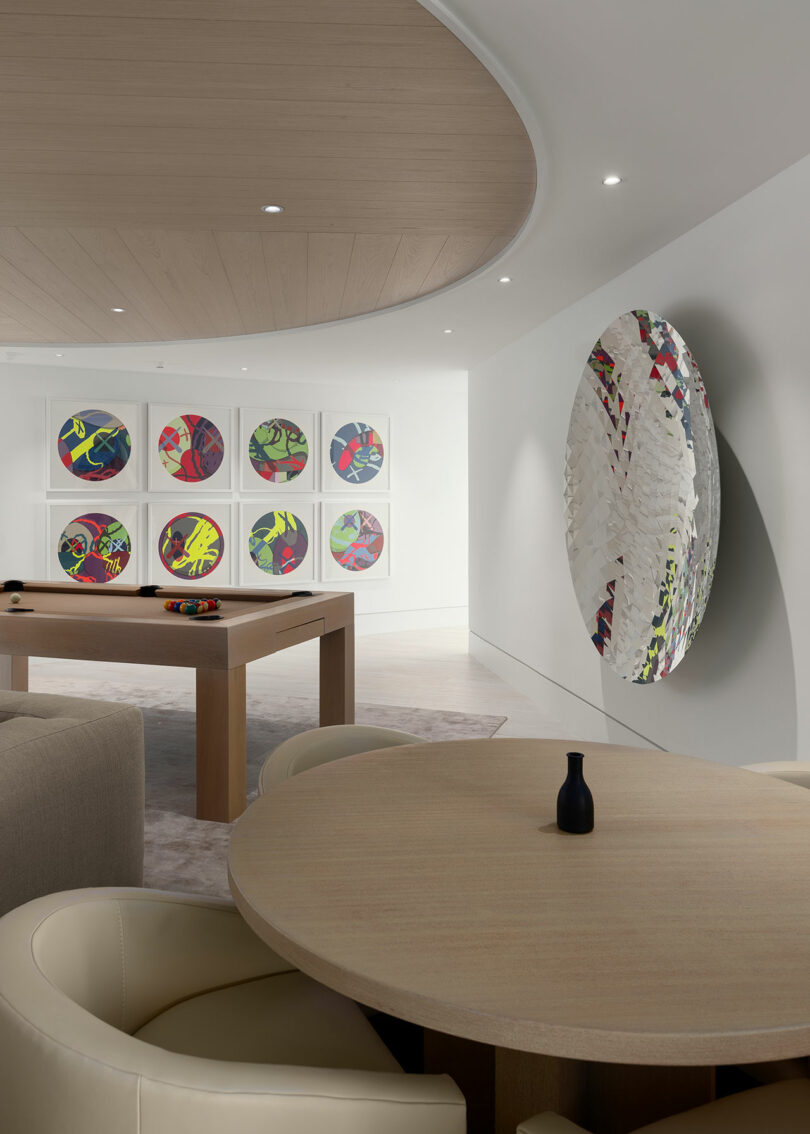 Modern room with circular wall art, a pool table, beige sofas, and a round wooden table with a small black vase. Neutral color palette and recessed lighting create a calm atmosphere.