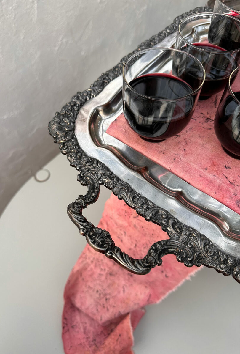 Ornate silver tray with glasses of red wine, resting on a draped pink cloth.