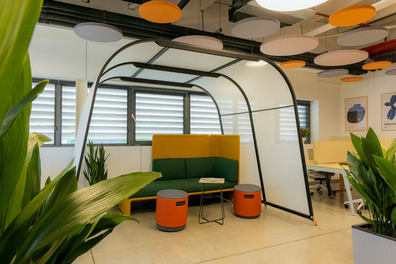 Modern office space with a small seating area under a curved frame, green plants, and circular ceiling panels.