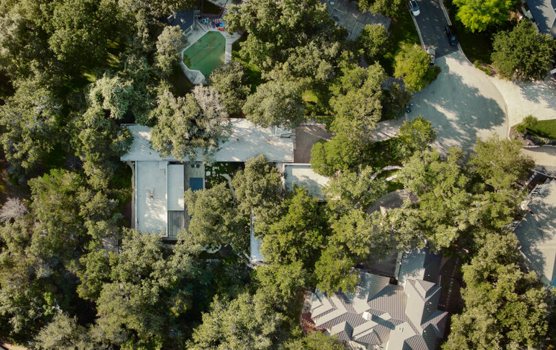 Vista aérea de una zona residencial con casas cubiertas de árboles y una pequeña piscina, rodeada de vegetación y caminos sinuosos.