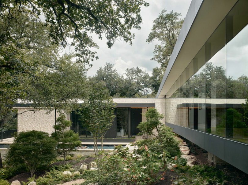 Modern building with large glass windows, surrounded by trees and landscaped gardens. Overcast sky in the background.