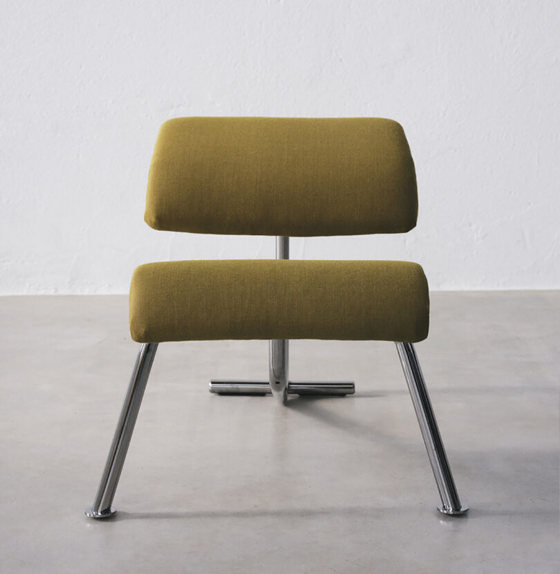 Modern chair with green upholstery and sleek metal legs, positioned against a plain white wall on a smooth floor.