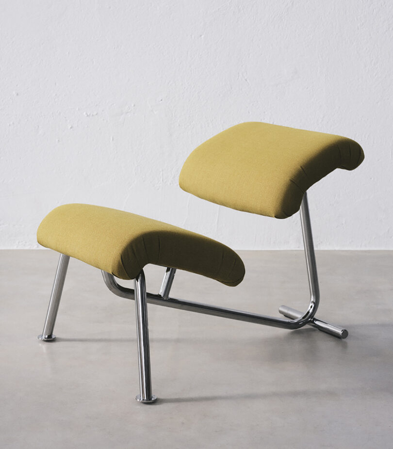 A modern chair with mustard-yellow cushions and a sleek metal frame, featuring a distinctive angled design, positioned on a light grey floor.