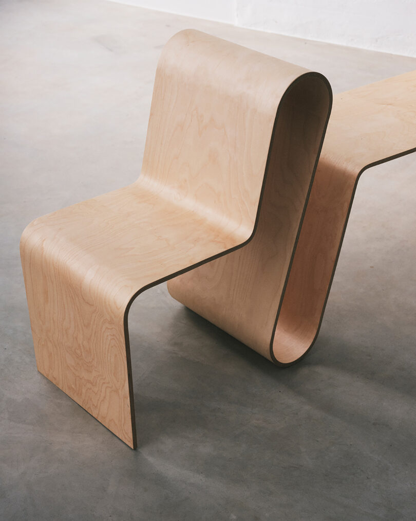 Curved wooden chair with a continuous flowing design on a smooth gray floor.