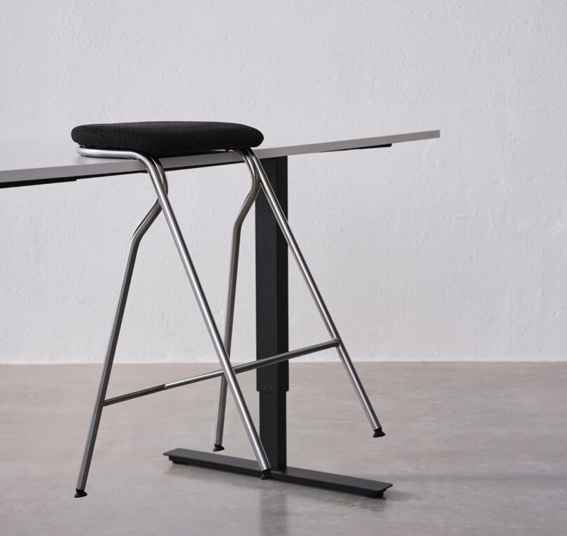 A sleek bar stool with a black cushioned seat and metal legs is positioned next to a minimalist table in a modern setting.