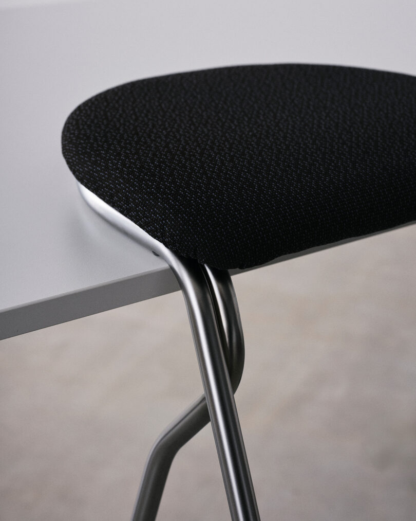 Close-up of a black upholstered chair seat with chrome legs, partially tucked under a white table.